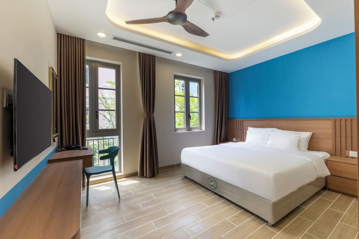 Een hotelkamer met een bed, een bureau met stoel, een televisie en een plafondventilator.