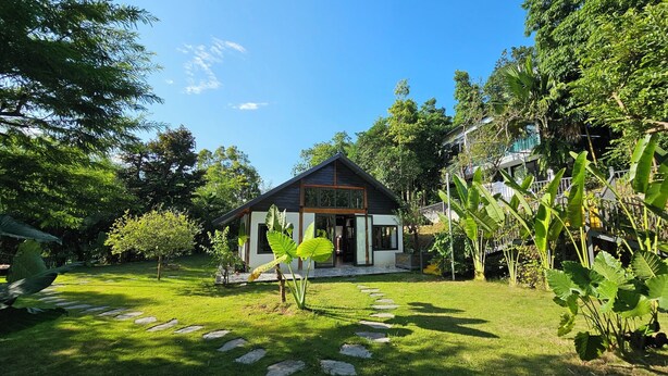 Une maison avec un chemin de jardin menant à l’entrée, entourée d’une végétation luxuriante et d’arbres.