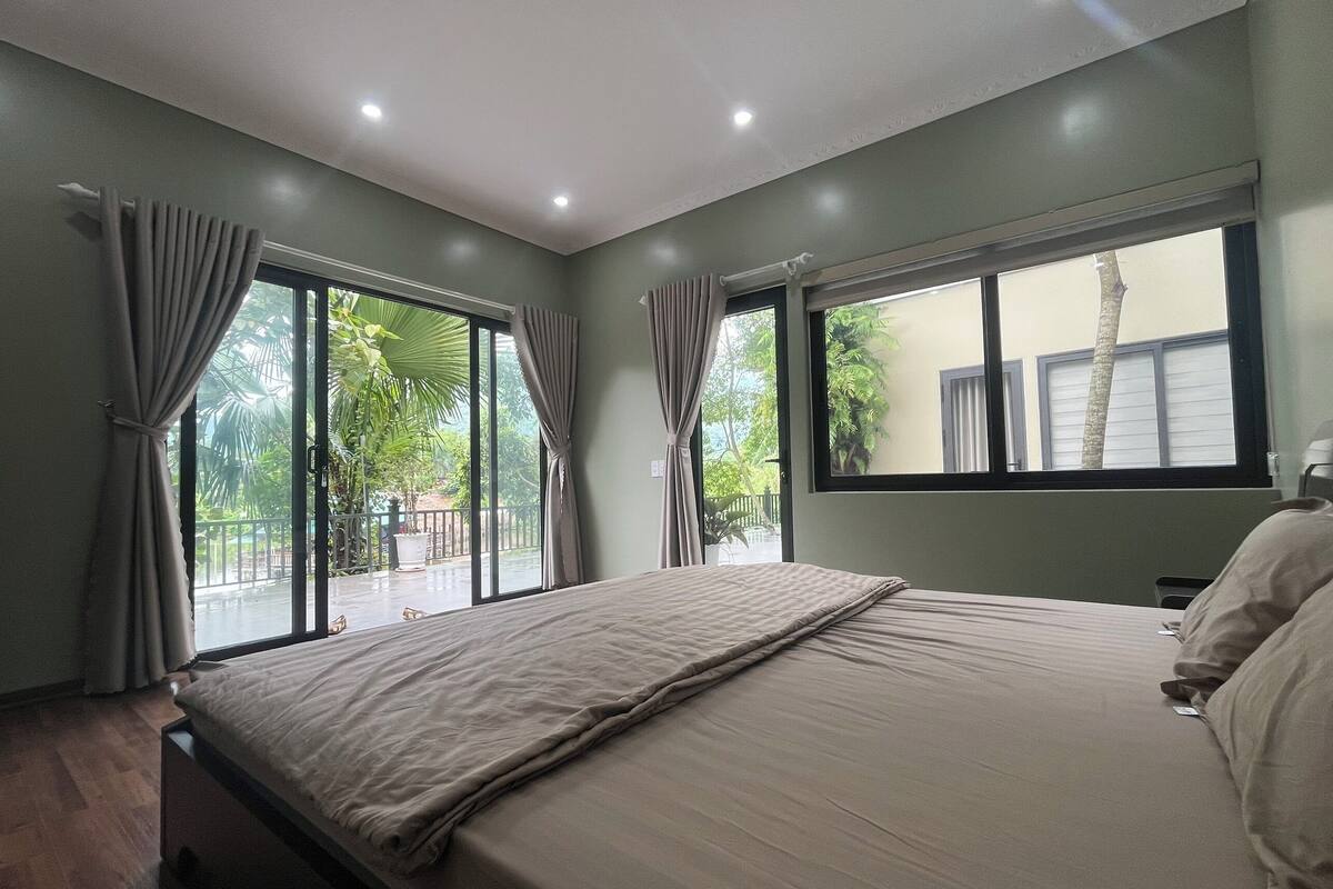 A bedroom with a bed, curtains, a window, and a view of greenery outside.