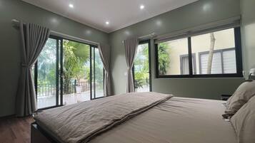 Een slaapkamer met een bed, gordijnen, een raam en uitzicht op groen.
