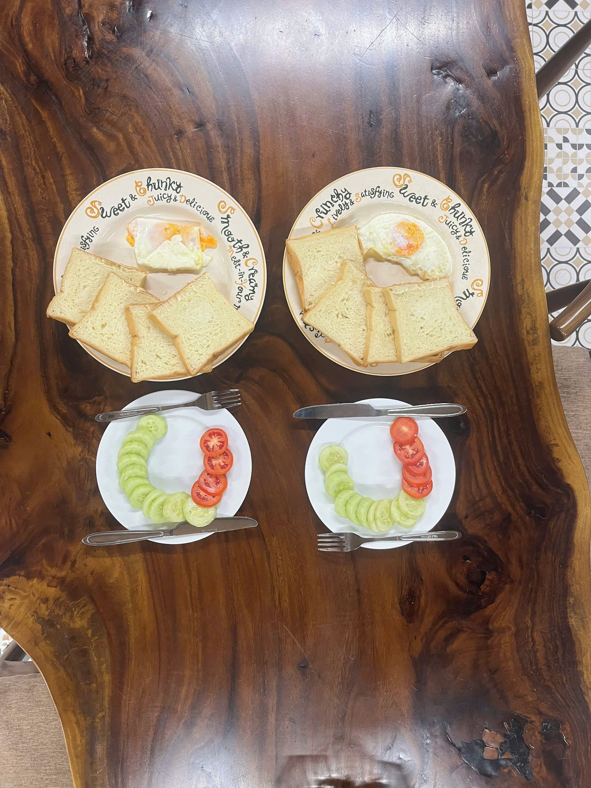 A wooden table with four plates of food, each with a different arrangement of bread, eggs, and vegetables.