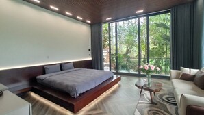 Une chambre moderne avec un grand lit, un canapé et une vue sur la verdure grâce à de grandes fenêtres.