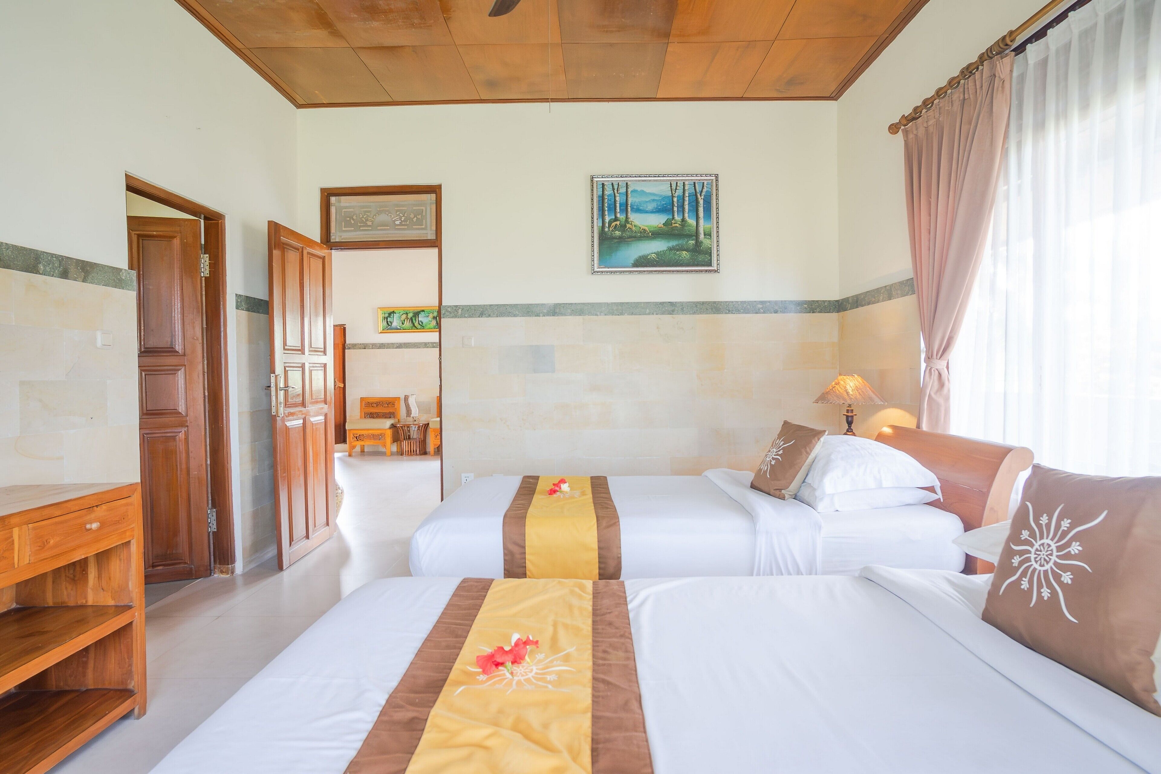 A hotel room with two beds, wooden furniture, a painting on the wall, and a window with curtains.