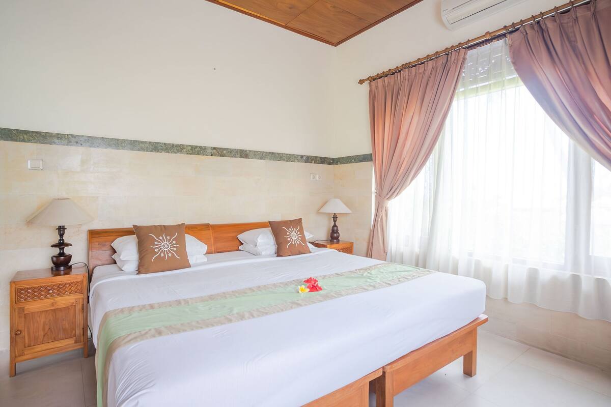 A neatly made bed with a green and white bedspread, two nightstands with lamps, and a window with curtains.