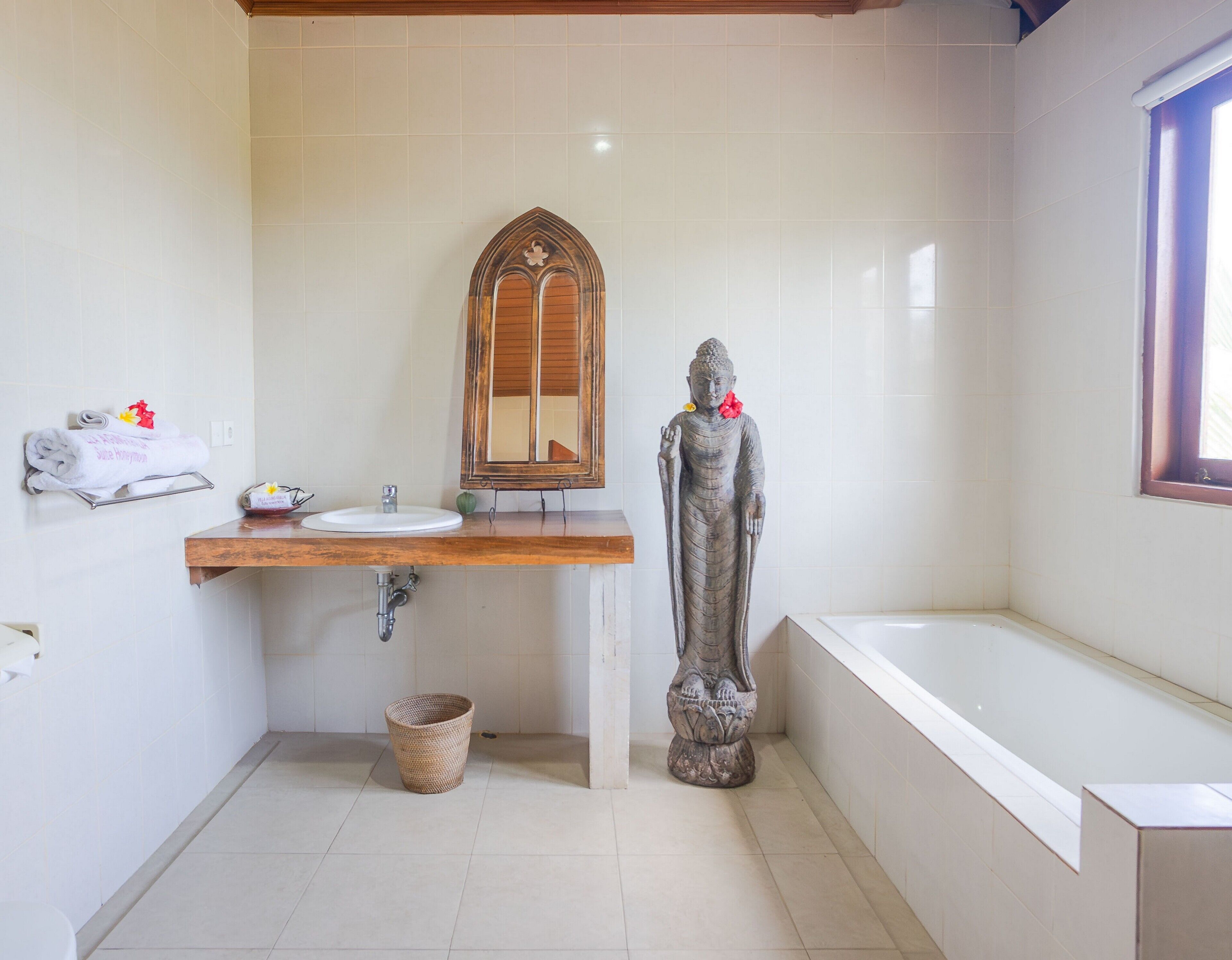 A bathroom with a wooden vanity, a sink, a mirror, a statue, and a bathtub.