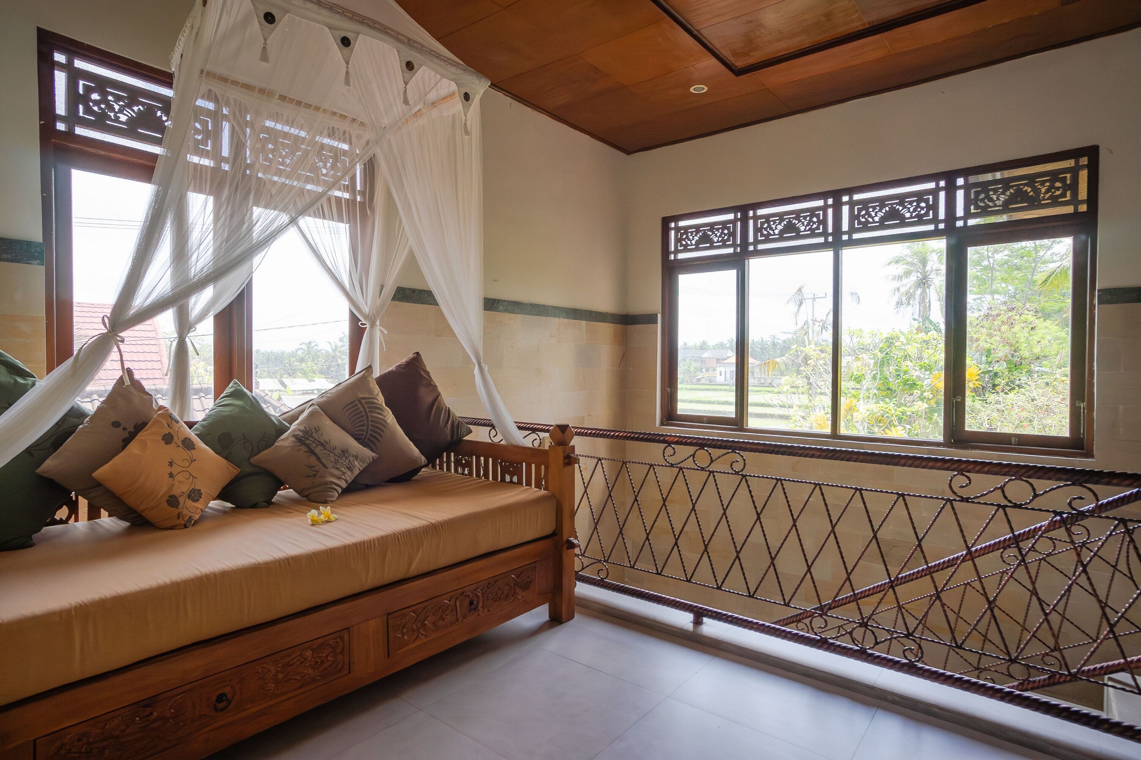 Una habitación con cama, ventana con vista a la vegetación y barandilla de balcón.