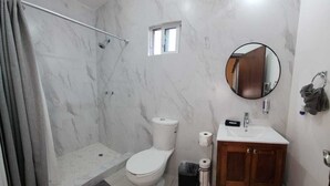 Un baño con ducha, inodoro, lavabo y un pequeño ventanal.