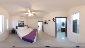Un dormitorio amplio con una cama grande, un ventilador de techo y vistas al baño a través de una puerta abierta.