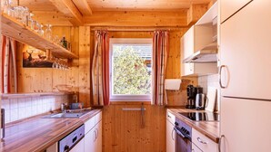 A compact kitchen with wooden walls, a window with curtains, and basic appliances. - Majestic chalet with terrace (Stadl an der mur)