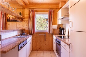 Eine kleine Küche mit Holzwänden, einem Fenster mit Vorhängen und einfachen Geräten.