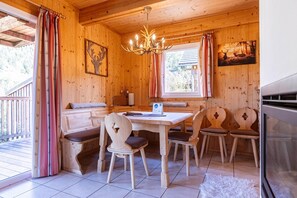 Interior de uma cabana de madeira com uma mesa de jantar, cadeiras, um banco, um candelabro e uma lareira.