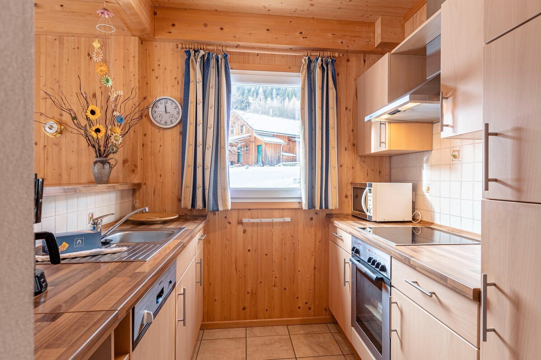 Een kleine keuken met houten kastjes, een spoelbak, een magnetron en een fornuis.