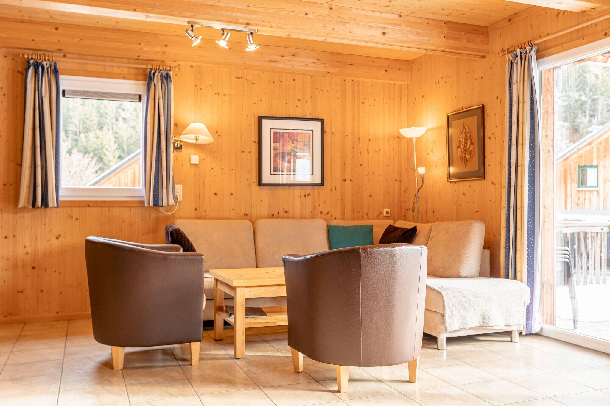 Een houten interieur met een bank, twee fauteuils, een tafel en een raam met gordijnen.