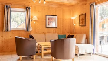 Een houten interieur met een bank, twee fauteuils, een tafel en een raam met gordijnen.