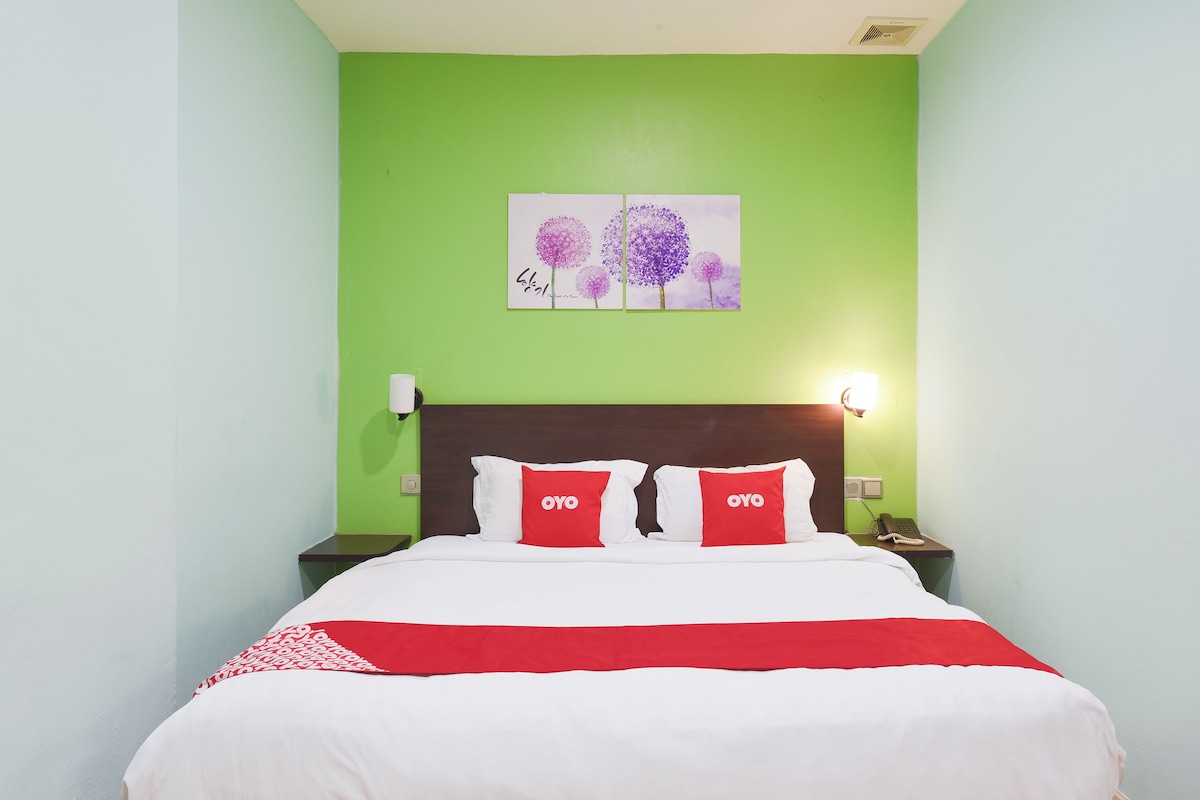 Une chambre d’hôtel avec un lit, des murs verts, un tableau représentant des arbres et une couvre-lit rouge et blanche.