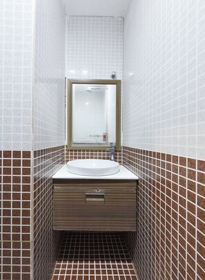 Un baño con un lavamanos blanco, un espejo y baldosas marrones con estampado.
