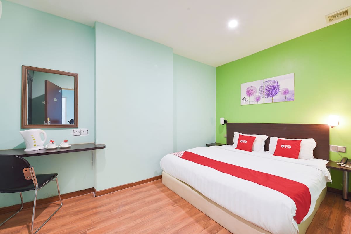 A hotel room with a bed, a desk, a chair, and a painting on the wall.