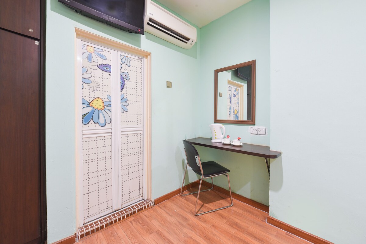 A small room with a wooden floor, a desk with a chair, a mirror, and an air conditioning unit.