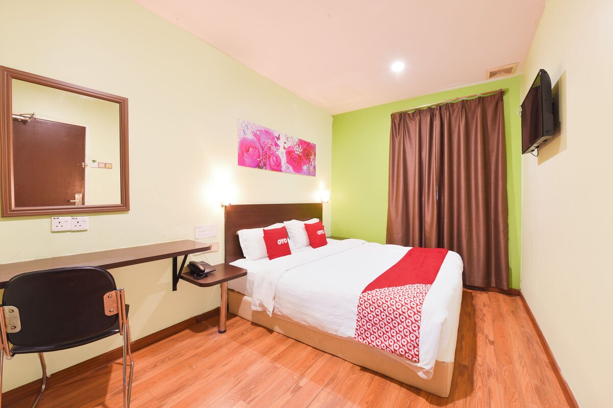 A hotel room with a bed, a desk, a chair, a TV, and a painting on the wall.