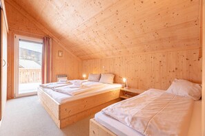 A wooden cabin bedroom with two beds, a sliding glass door to a balcony, and a small bedside table with a lamp. - Lovely chalet with sauna (Stadl an der mur)