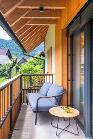 Un balcon doté d’un plancher en bois, d’un canapé gris et d’une petite table ronde sur laquelle se trouve une tasse verte.