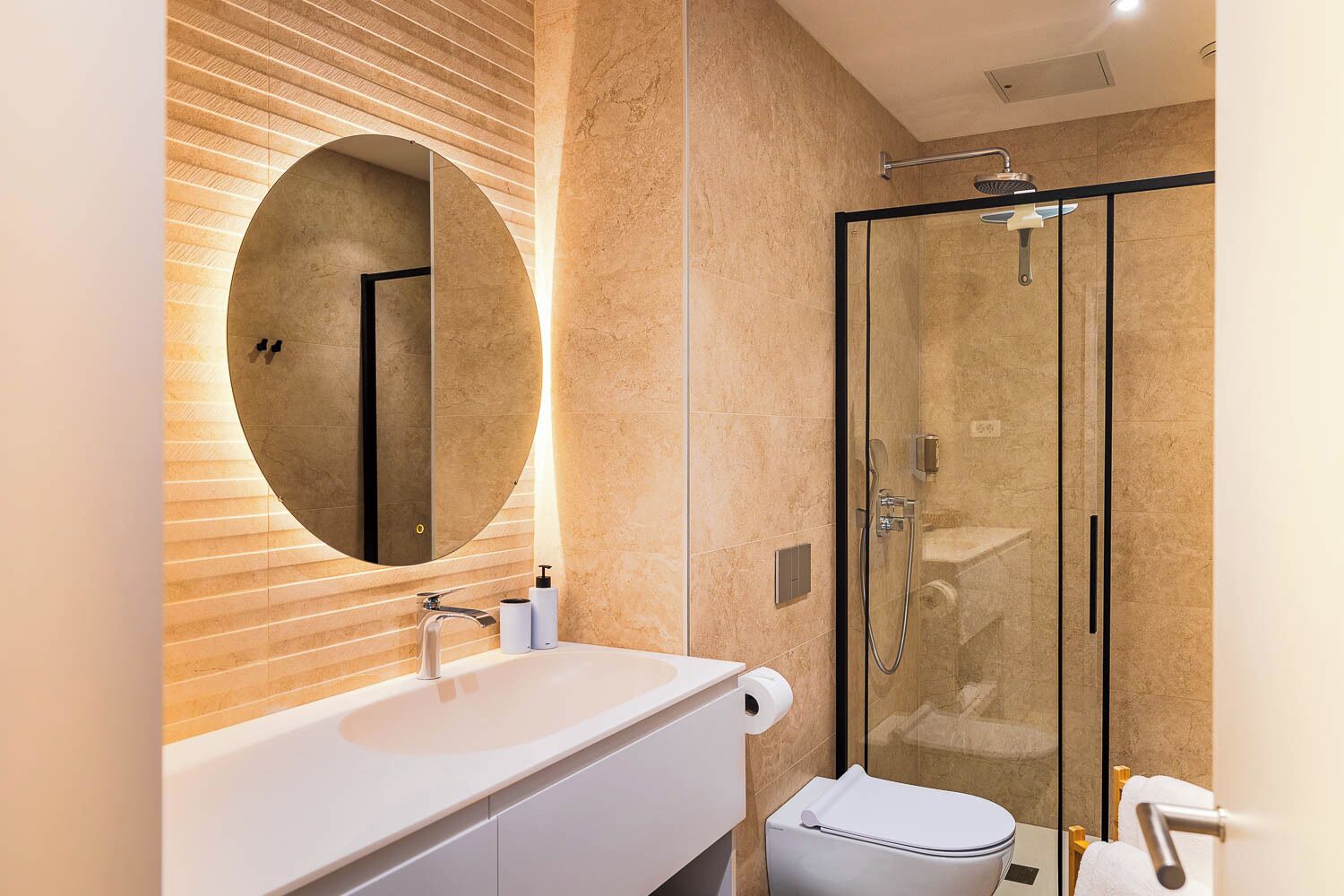 A modern bathroom with a round mirror, a white sink, and a glass-enclosed shower.