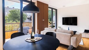 A modern living room with a large window, a dining table with chairs, a sofa, and a TV mounted on the wall. - Vila Nina Bohinj (Bohinj)