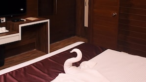 Habitación de hotel con techo de madera, cama con almohada en forma de cisne blanco, televisor sobre un mueble blanco y aire acondicionado de pared.