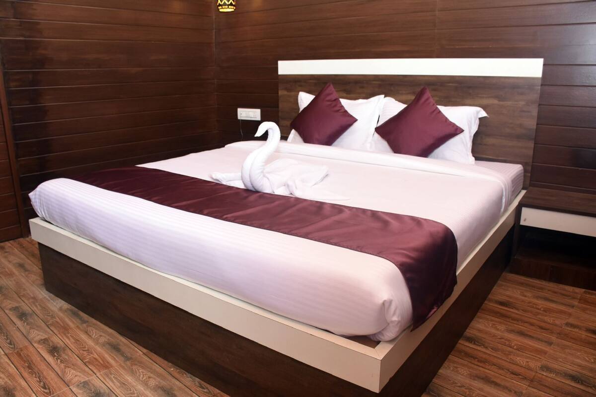 A double bed with a white headboard and two pillows, a dark red bedspread, and a swan-shaped towel.
