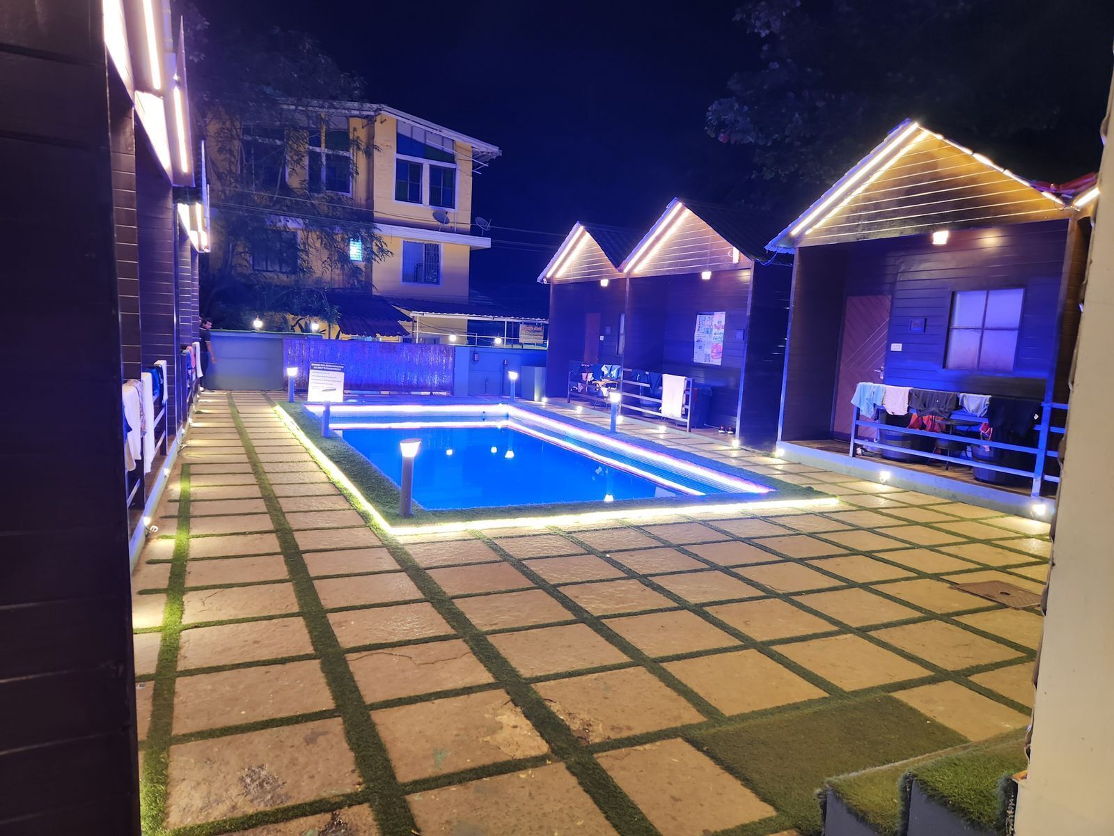 A swimming pool with surrounding lounge areas, a covered seating area, and a building in the background.