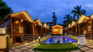 Un resort con cabañas de madera, una piscina central y palmeras al fondo.
