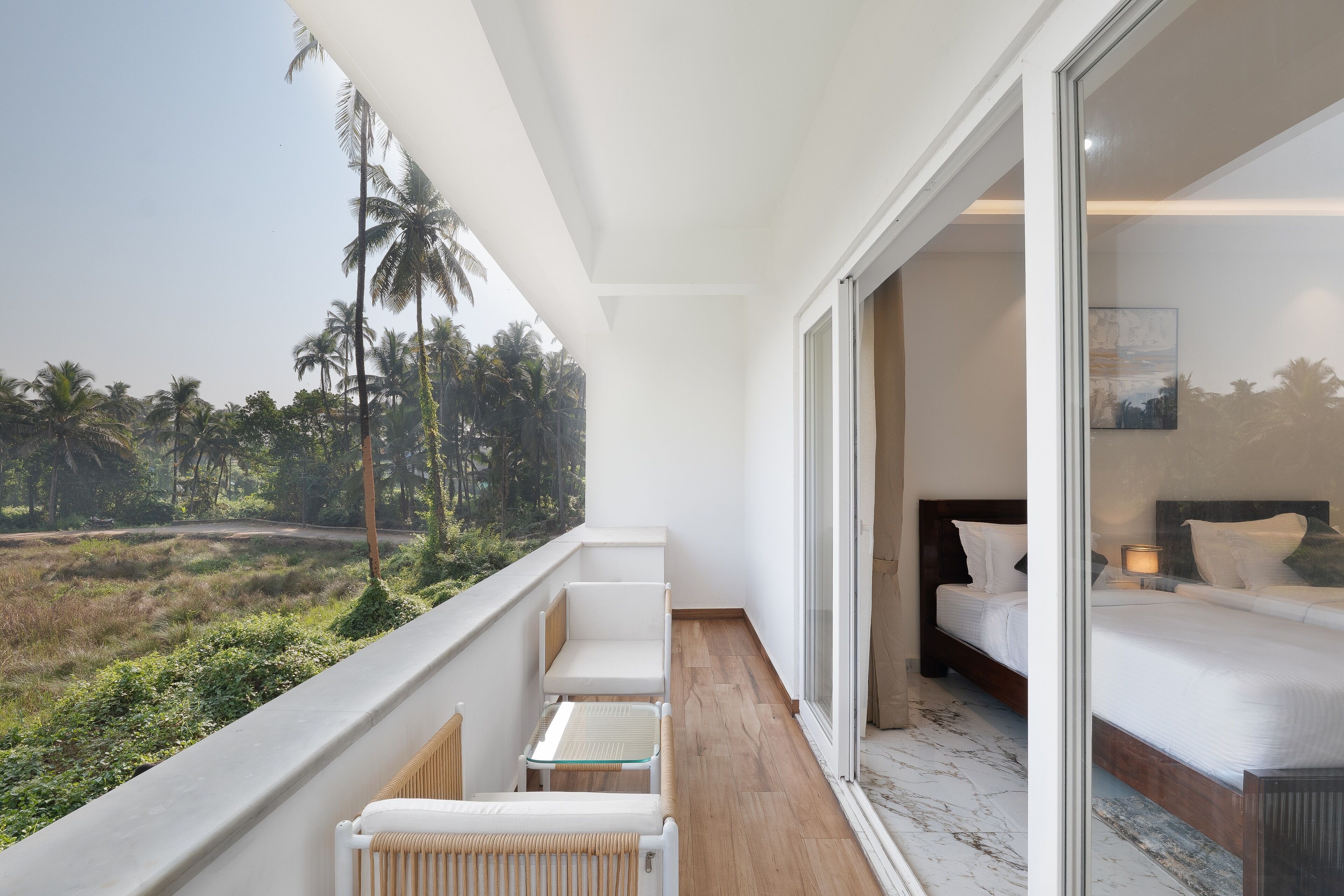 A balcony with a view of palm trees and a bed with a wooden headboard inside the room.