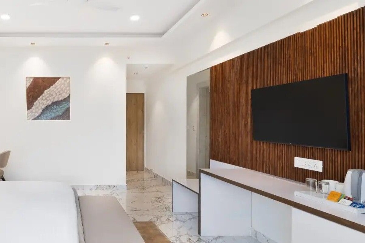 A modern hotel room with a large bed, a desk with a lamp, a TV mounted on the wall, and a wooden panel design.