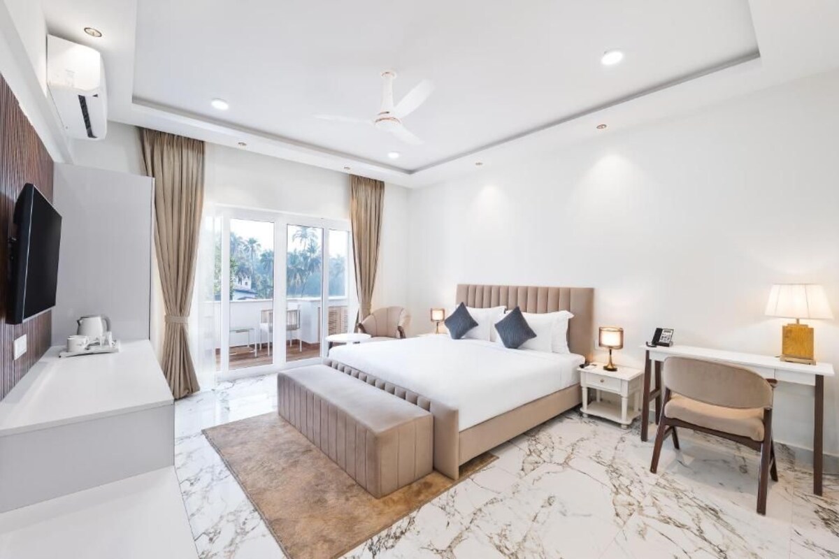 Una habitación de hotel moderna con una cama grande, un escritorio, una silla, un televisor y un balcón con cortinas.