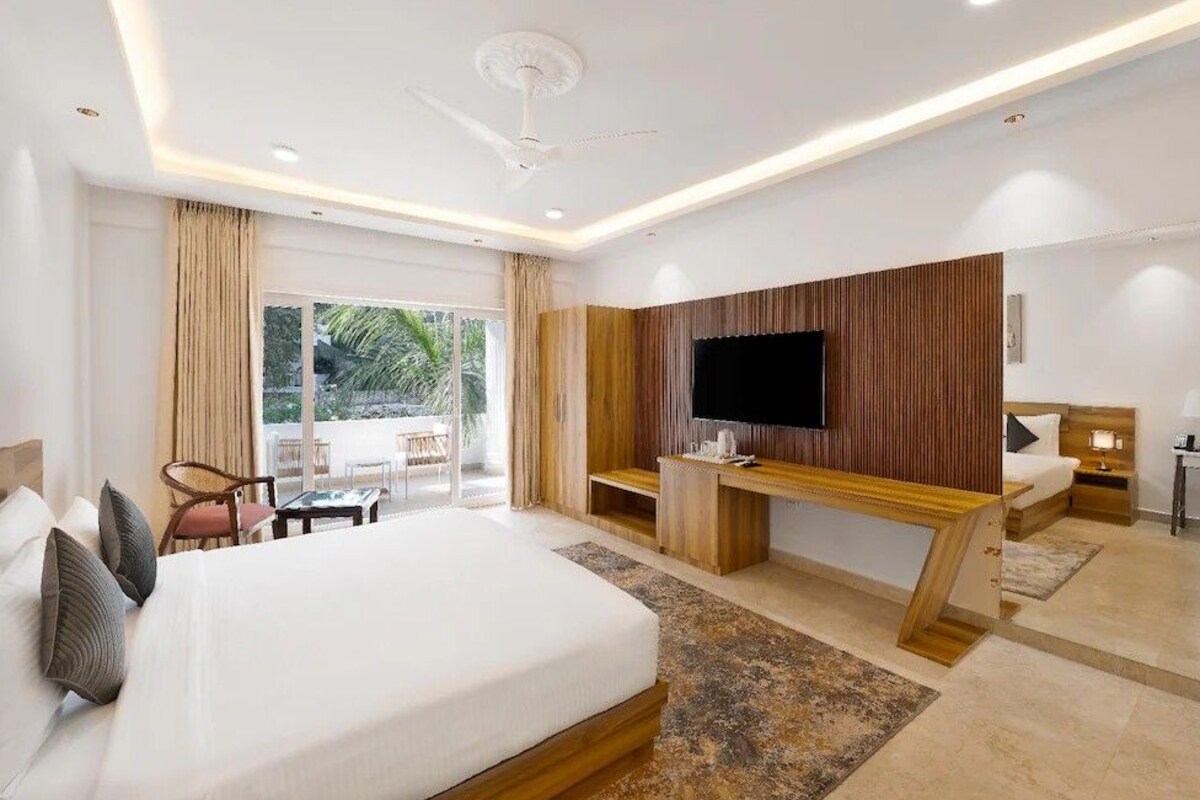 Una habitación de hotel moderna con una cama grande, un escritorio, un televisor de pantalla plana y un balcón con mobiliario exterior.
