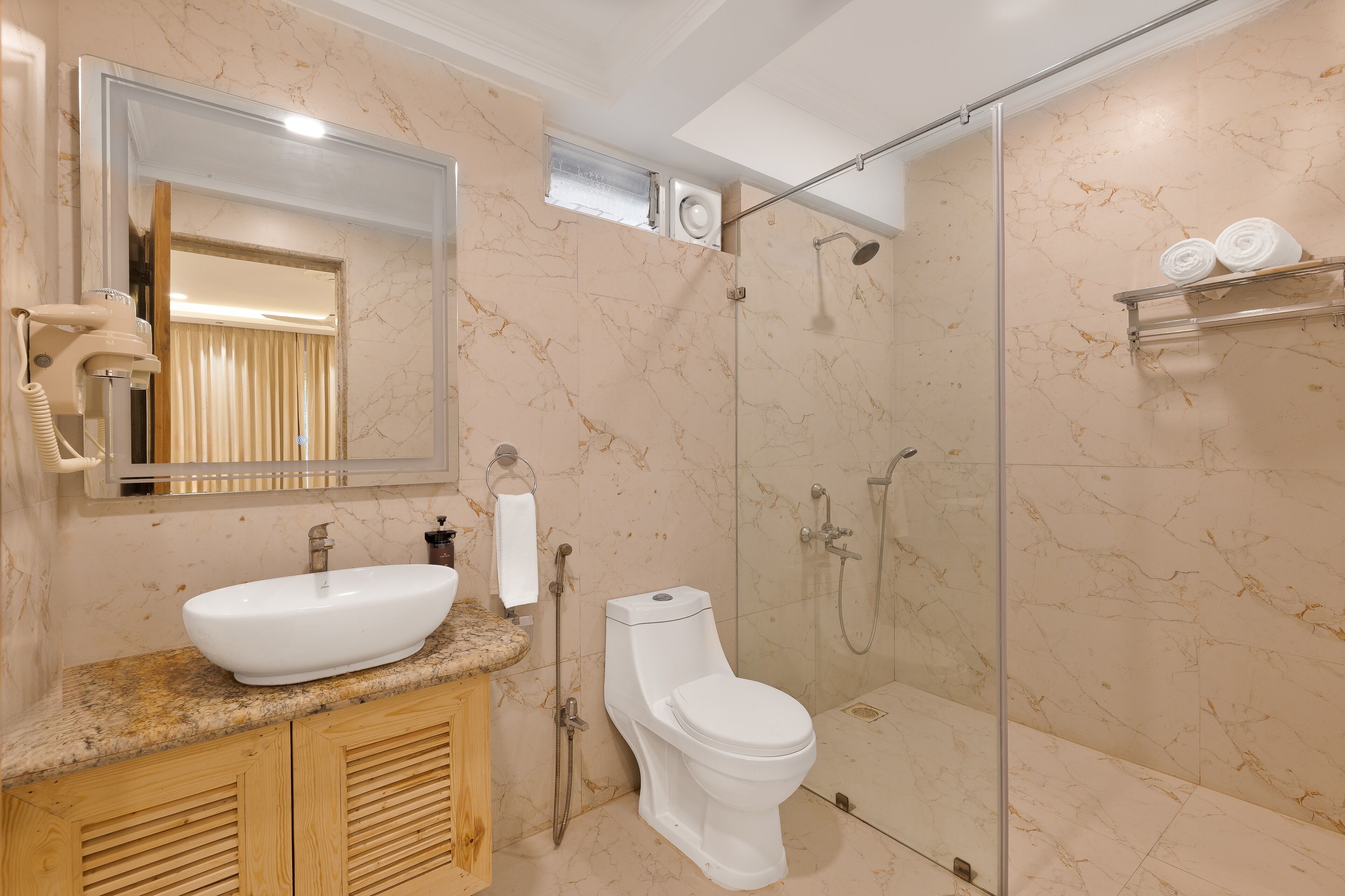 A bathroom with a marble vanity, a white sink, a toilet, a glass-enclosed shower, and a towel rack.