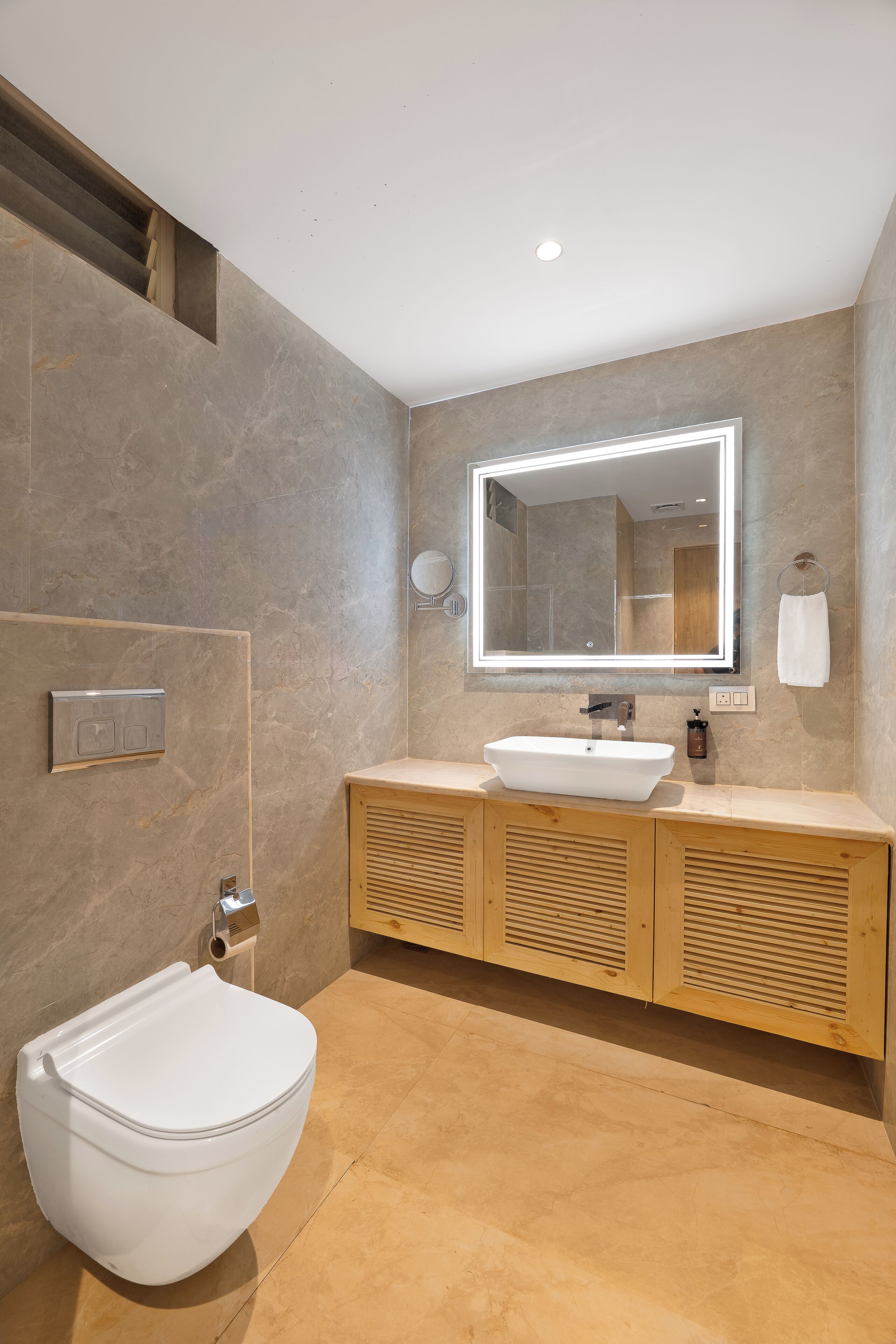 A modern bathroom with a white toilet, a large mirror, and a wooden vanity.
