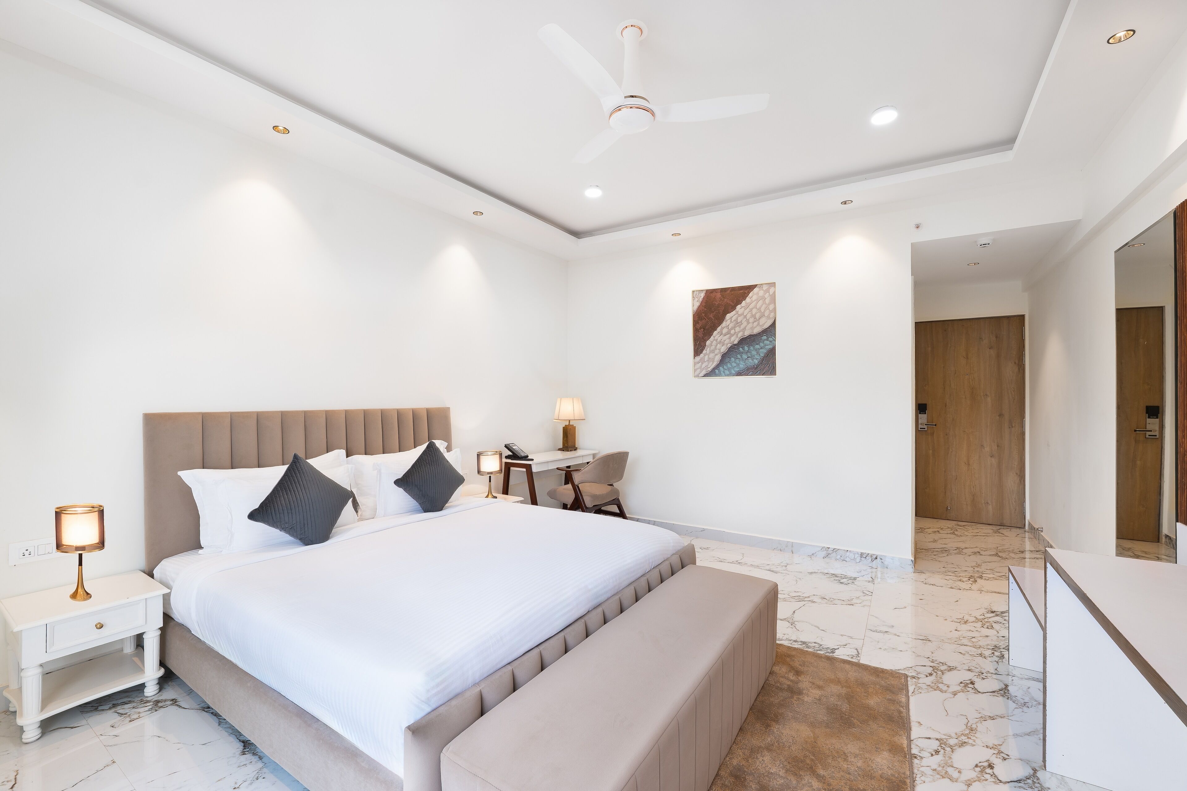 A modern hotel room with a large bed, bedside tables, a desk, and a seating area.