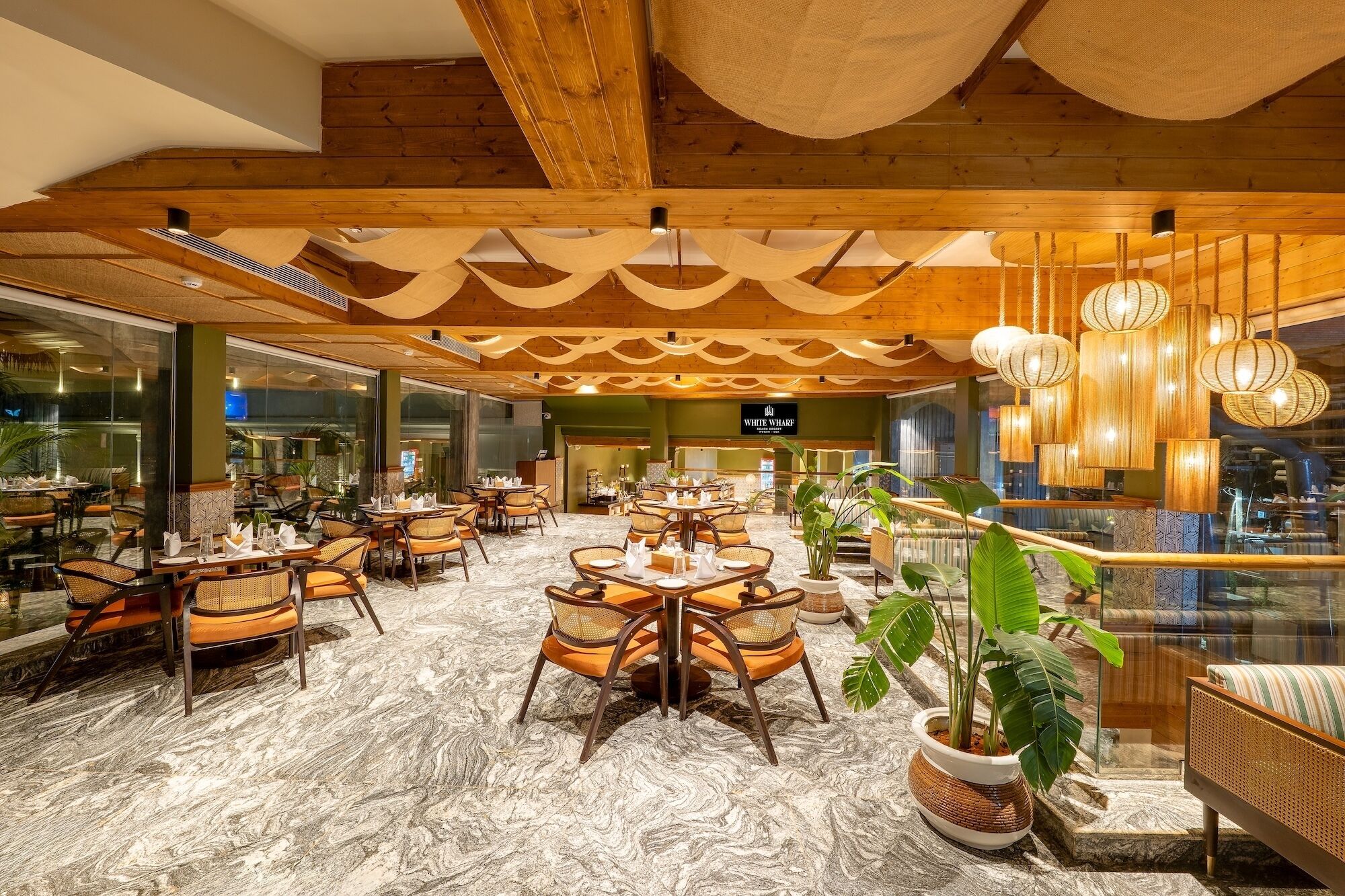 A spacious indoor dining area with wooden ceiling beams, hanging lanterns, and a marble floor.