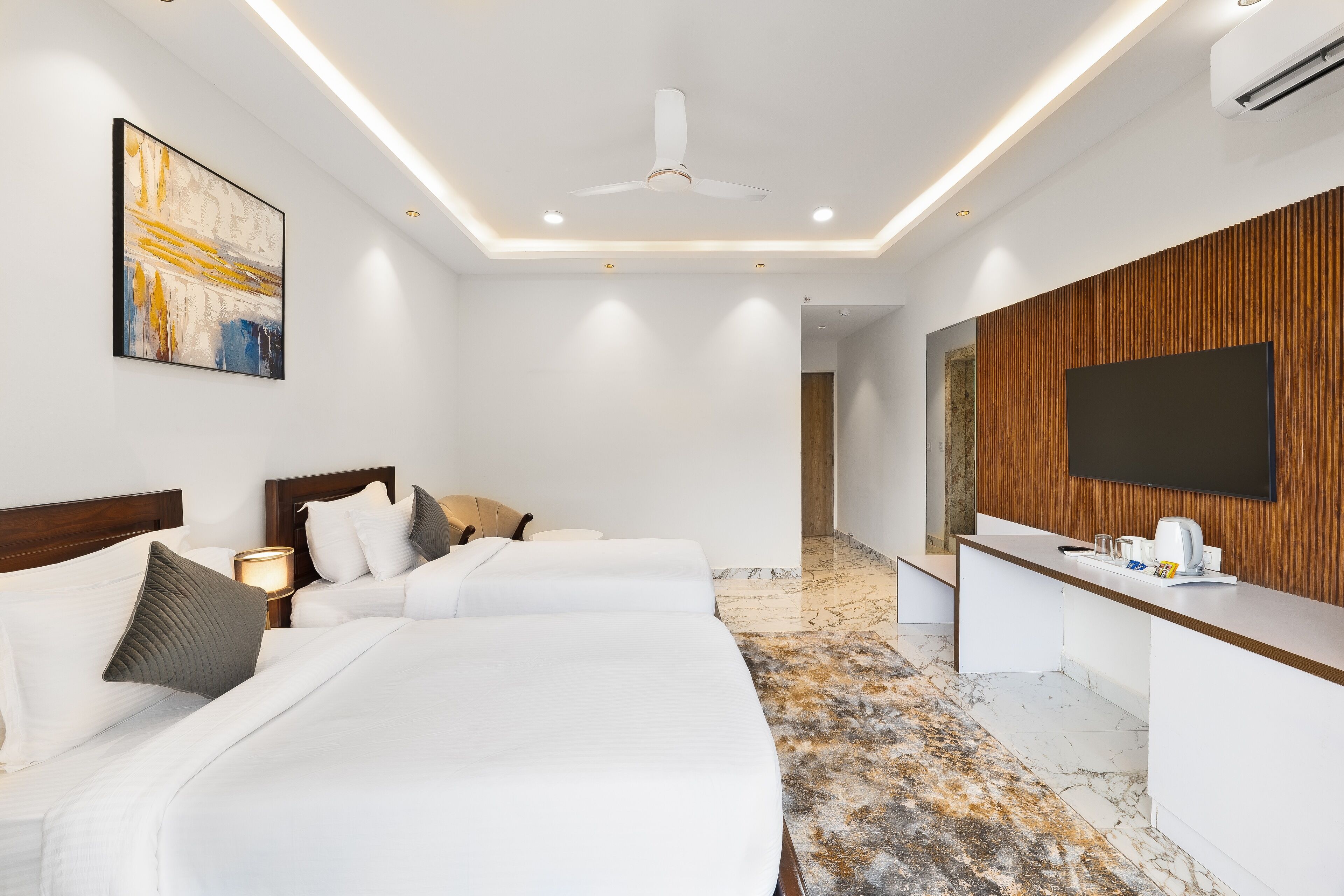 A hotel room with a large bed, a desk with a flat-screen TV, a ceiling fan, and a painting on the wall.