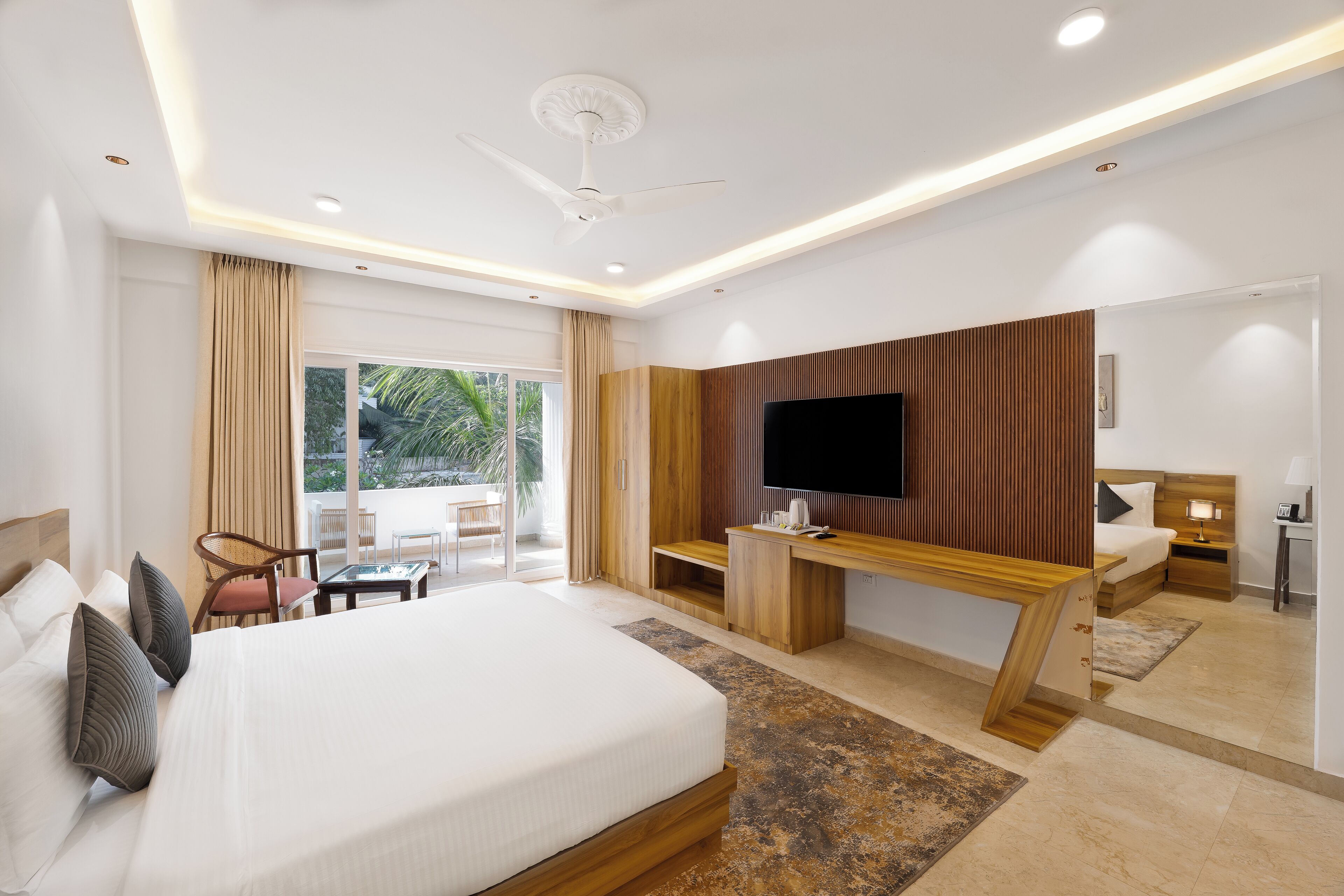 Una habitación de hotel moderna con una cama grande, un escritorio, un televisor y un balcón con vistas a zonas verdes.