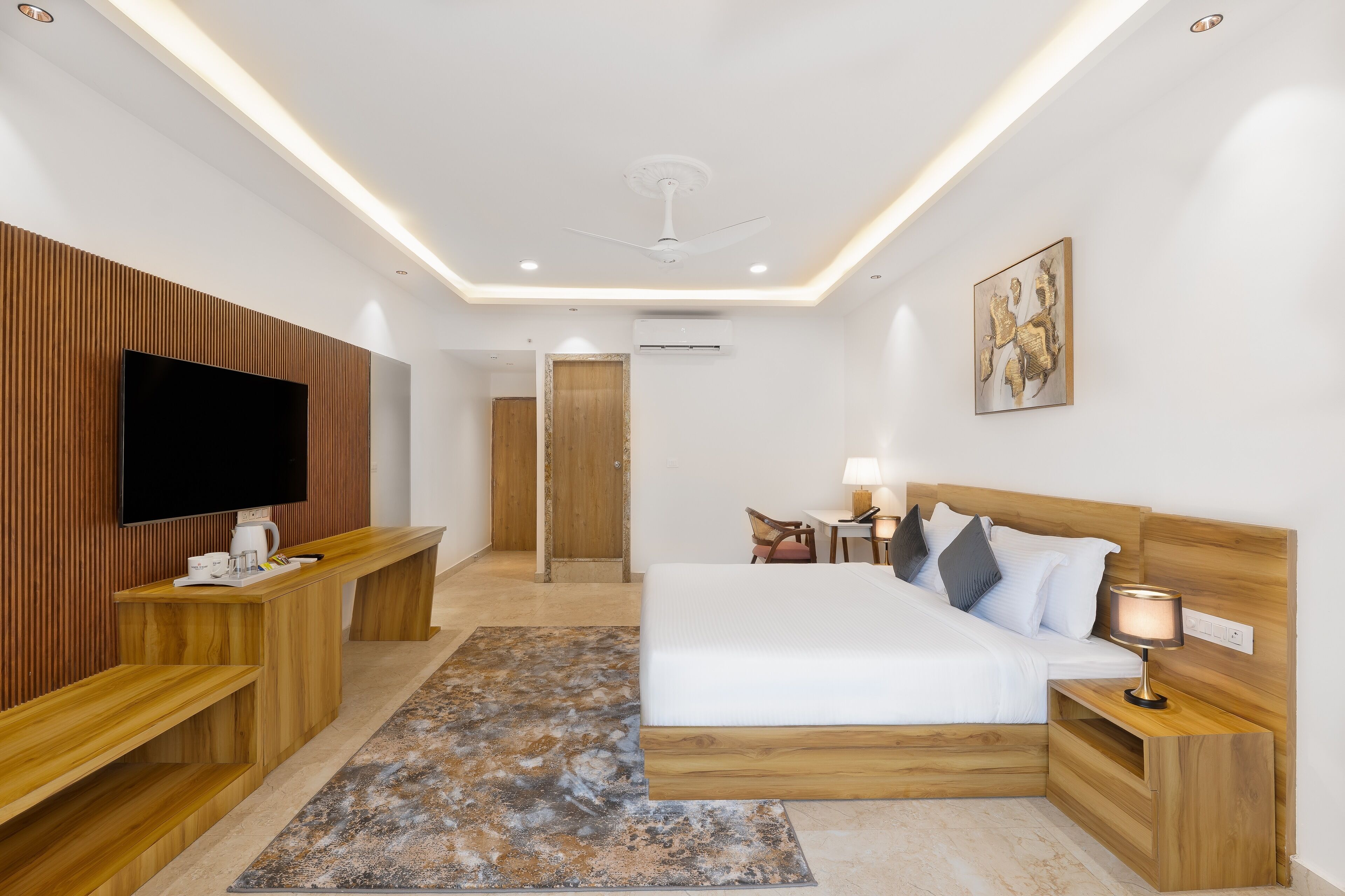 Una habitación de hotel moderna con una cama grande, muebles de madera, un televisor de pantalla plana y un ventilador de techo.