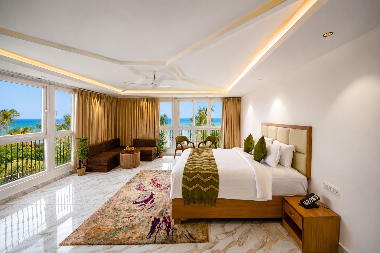 A hotel room with a large bed, a balcony with a view of the ocean, a seating area with a sofa and chairs, and a small table with a plant.