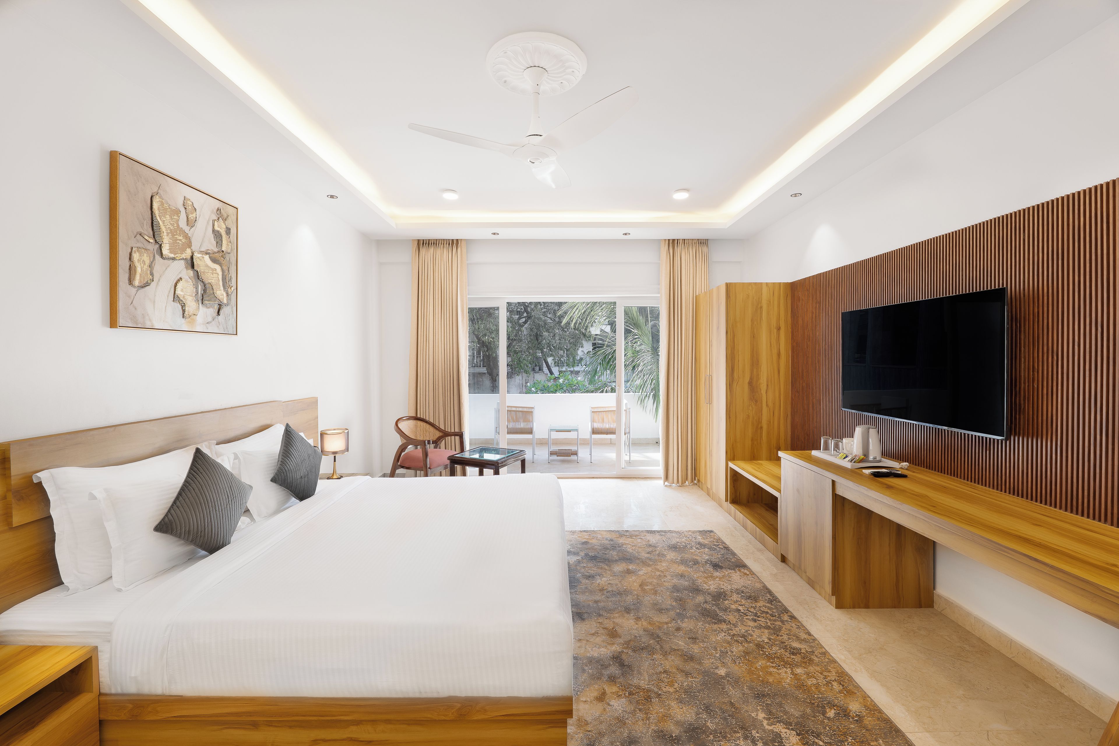 Ein modernes Hotelzimmer mit einem großen Bett, einem Flachbildfernseher, einem Holztisch und einem Balkon mit Sitzgelegenheit.