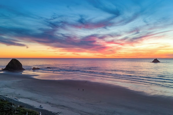Une plage où l’on peut admirer le coucher de soleil, avec une mer calme et des formations rocheuses.
