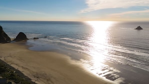 A beach with clear skies, calm waters, and rocky outcrops. - Arch Cape Retreat • Hot Tub • Near Cannon Beach + Haystack Rock | Royal Canoe (Arch Cape)