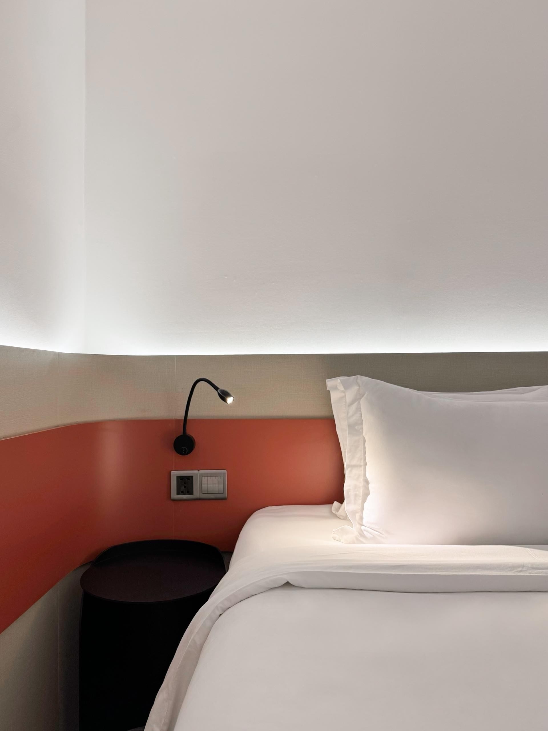 A hotel room with a neatly made bed, a bedside lamp, and a small nightstand.