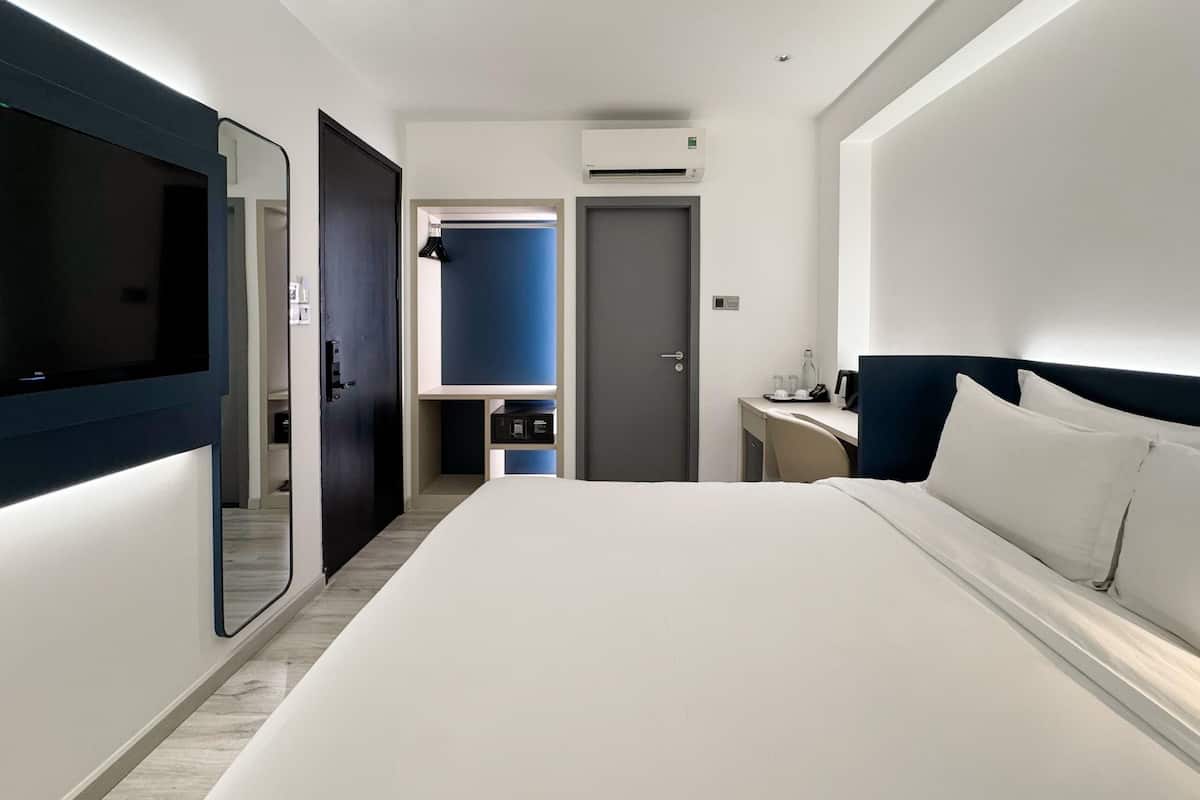 A modern hotel room with a large bed, a desk, a mirror, and a wardrobe.
