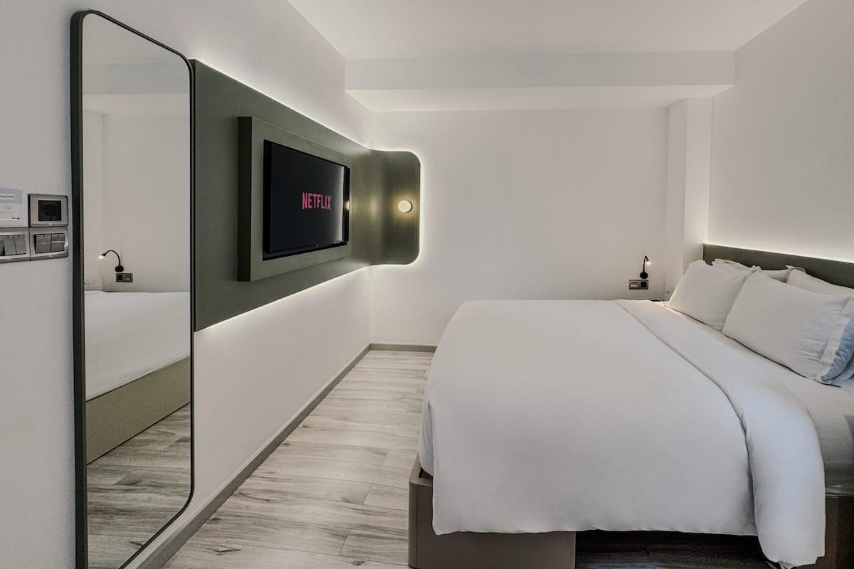 A modern hotel room with a large bed, a wall-mounted TV, and a mirror.