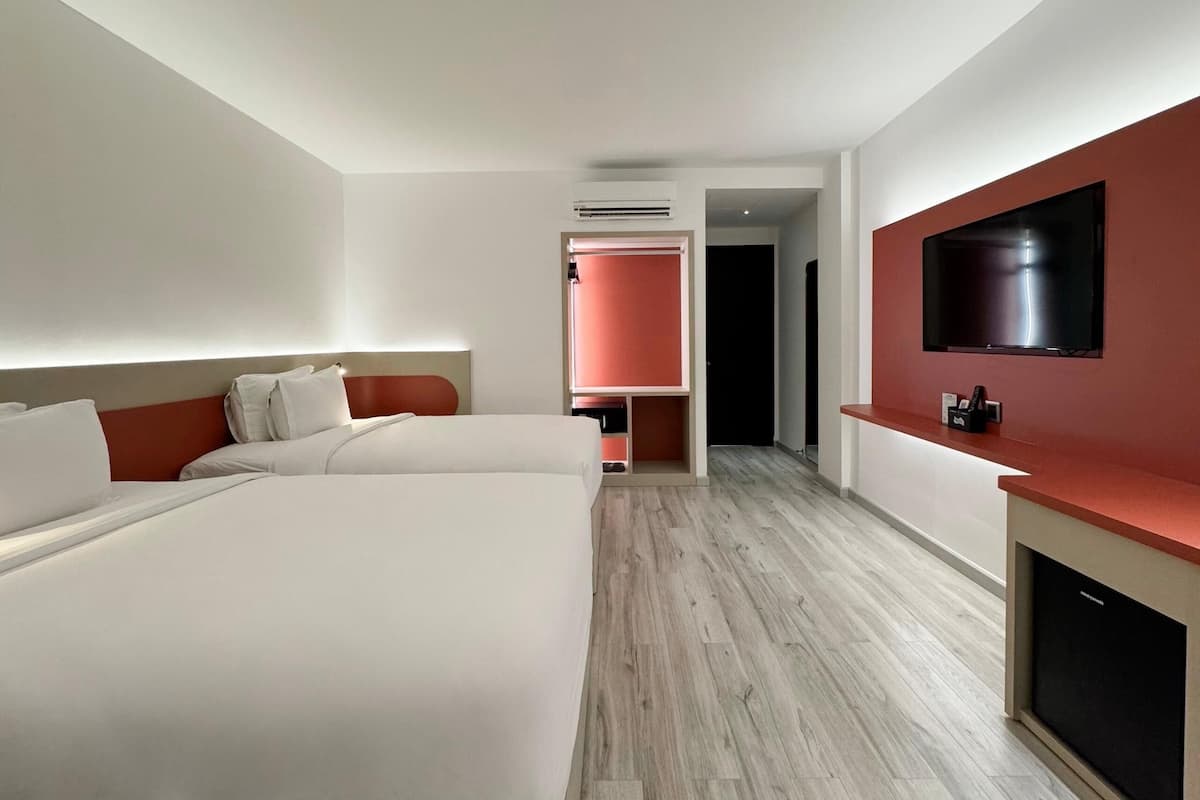 A hotel room with two beds, a TV mounted on the wall, and a red accent wall.